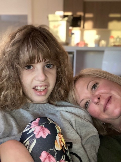 A woman resting her head on the shoulder of a teenage girl with red curly hair