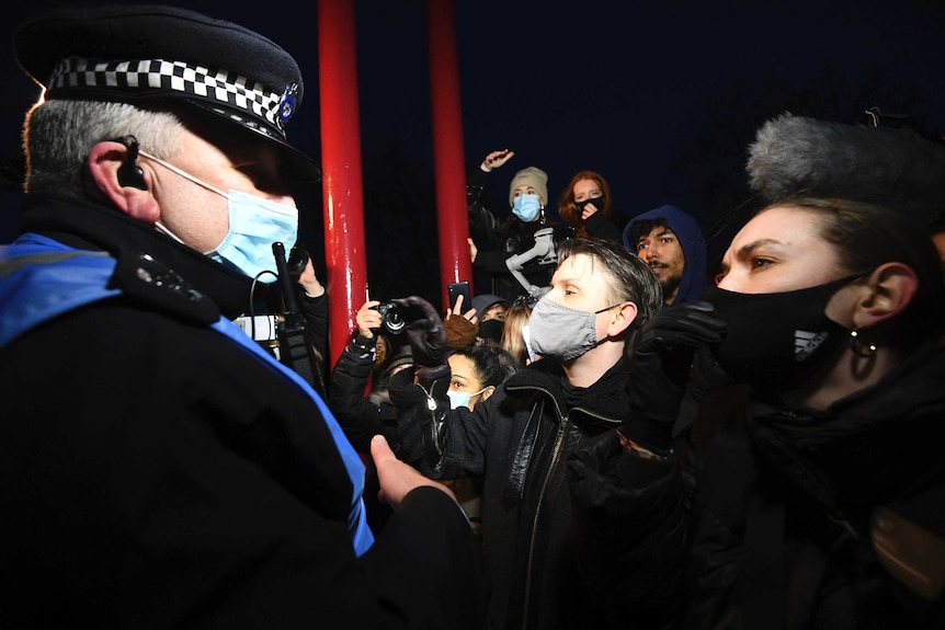 Un agent de police britannique debout devant un groupe de femmes portant des masques faciaux