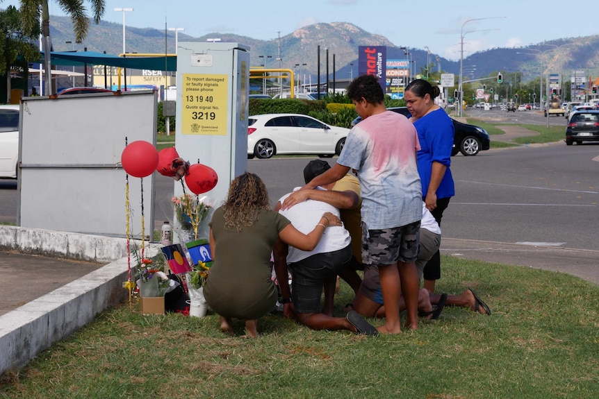 five people crowd around a makeshift memorial in Townsville