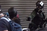 A police officer wearing riot gear and a mask pulls a gun towards another person.