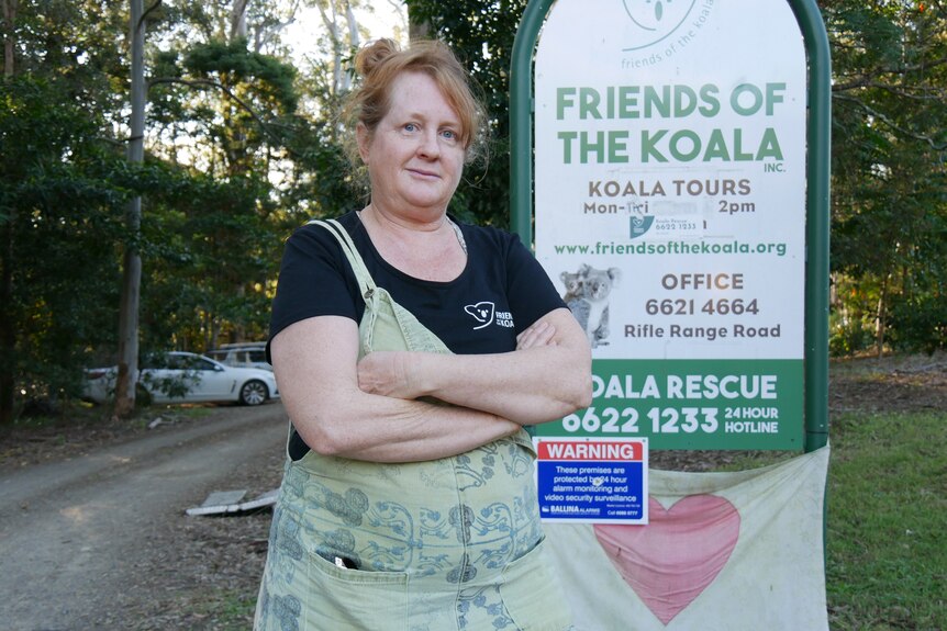 A woman in green overalls stands near a sign reading 'friends of the koala'.