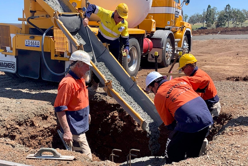 Men in high vis work gear pouring materials into a pit at a construction site.