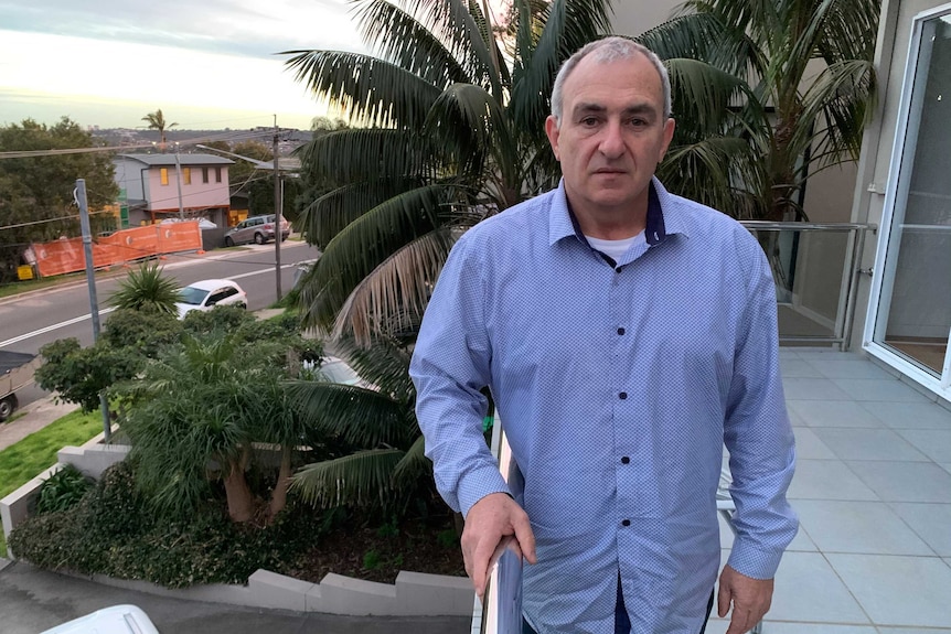 Bill Yeates wearing a blue patterned shirt, standing on a balcony at his home.