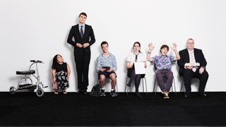 Six people standing and sitting against a white wall