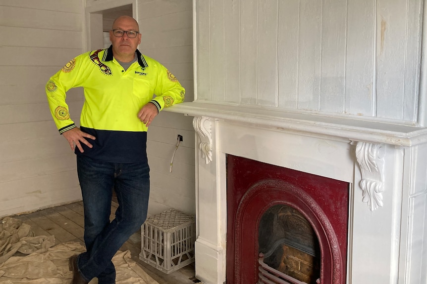 A man poses next to a fireplace