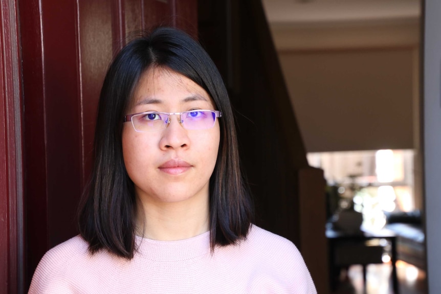 Mien Jeu Chang has a serious expression on her face as she stands in front of her door.