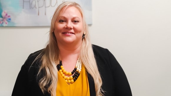 A smiling blonde woman wearing a bright shirt and a dark jacket.