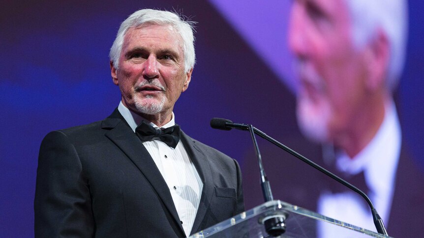 A former AFL coach speaks at a podium at an awards dinner.