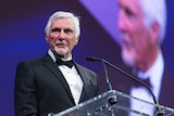 A former AFL coach speaks at a podium at an awards dinner.