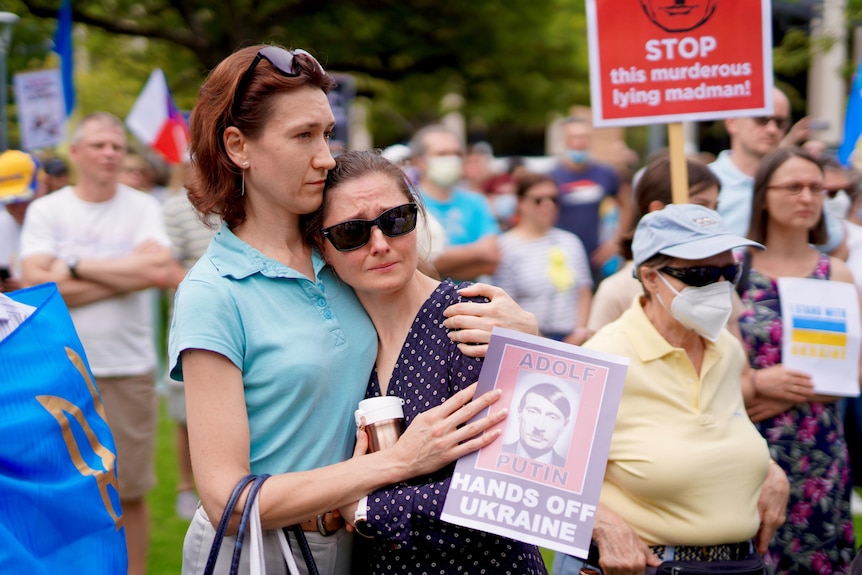 A woman holding a poster depicting Putin as Hitler consoles another woman