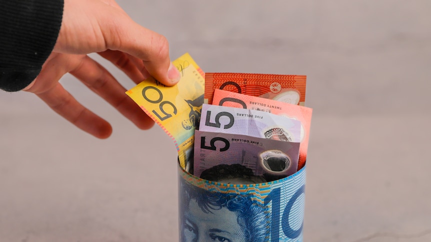 A hand pulls Australian dollars in notes out of a money box