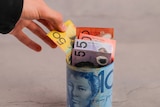 A hand pulls Australian dollars in notes out of a money box