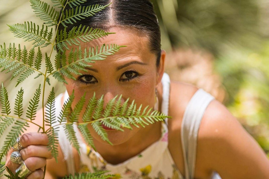 Poh Ling Yeow looking at camera through a piece of bracken