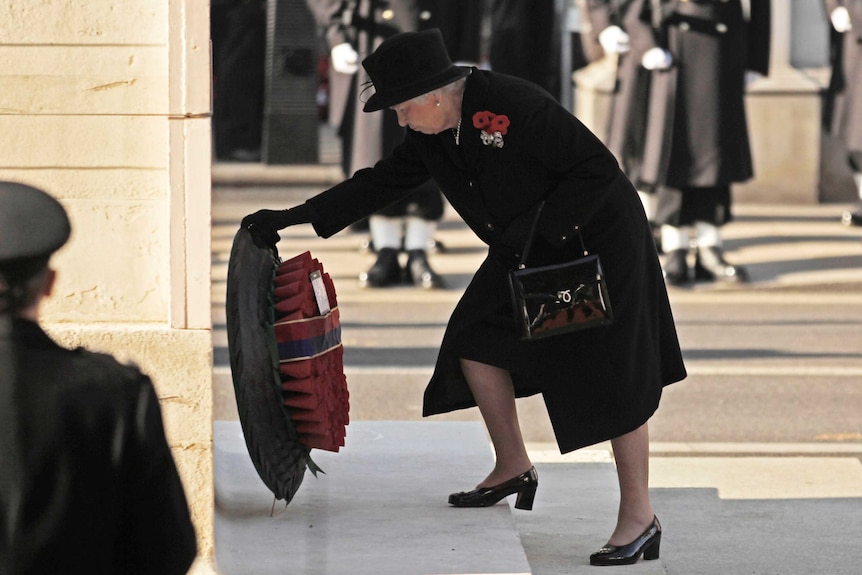 Queen Elizabeth is seen from side-on bending down to lay a wreath