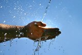 Water splashes onto a hand with sunlight in the background.