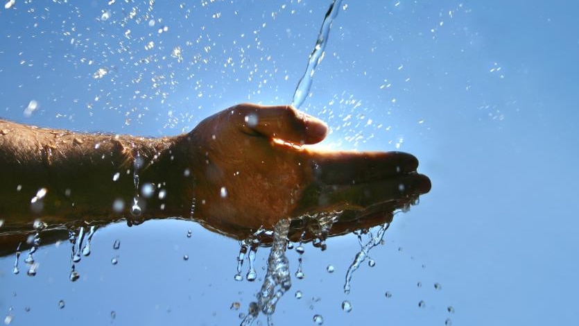 Water splashes onto a hand with sunlight in the background.