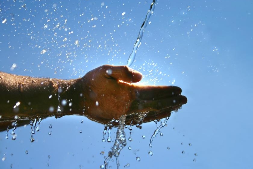 Water splashes onto a hand with sunlight in the background.