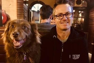 A man smiling next to his dog at a pub