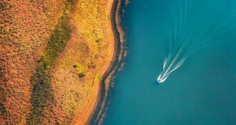 A boat speeds along a lake's edge as seen from above