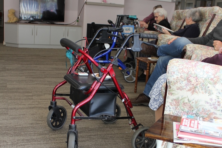 A line of walkers infront of chairs at an aged care home