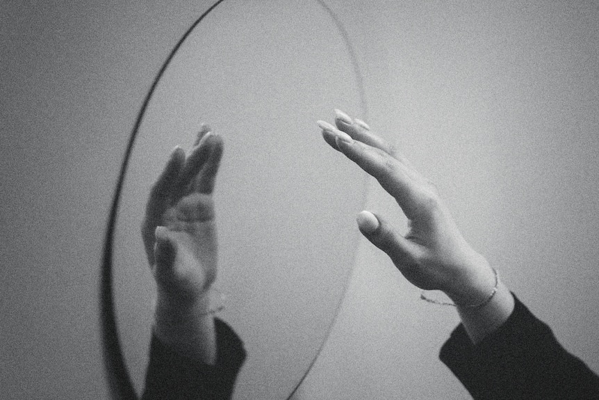Black and white image of a hand reaching to the mirror