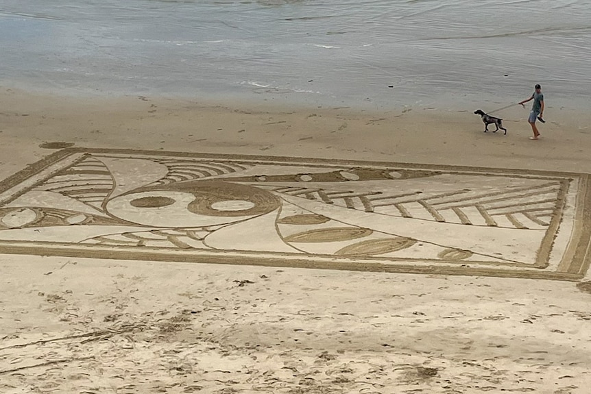 A large sand art design created on a beach, featuring line designs within a square shape.