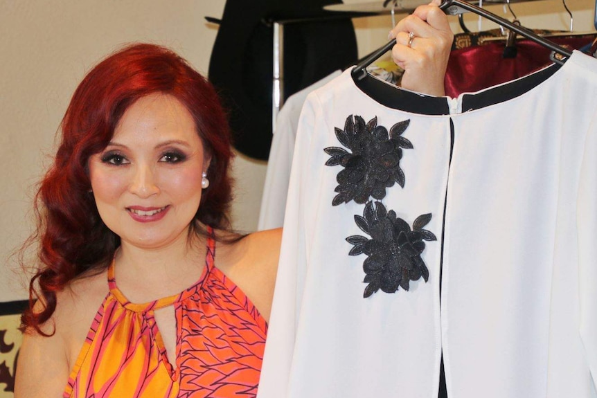 Sandra holds up one of her designs, a white long-sleeved shirt with black embroidered flower design.