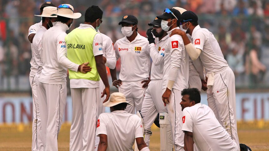 Sri Lanka's players, wearing anti-pollution masks, gather on the field.