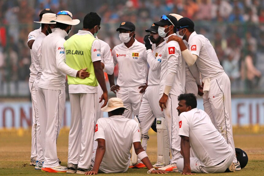 Sri Lanka's players, wearing anti-pollution masks, gather on the field.
