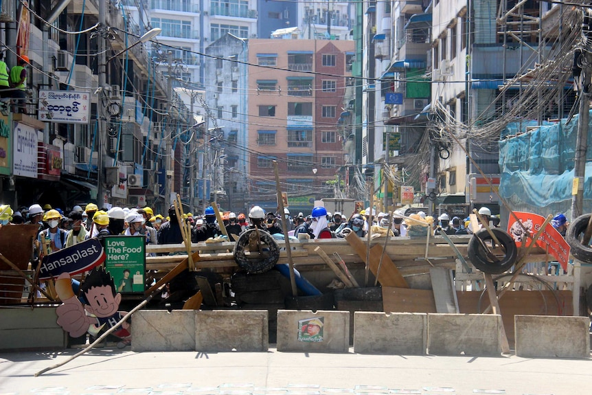 A huge crowd uses bit of timber, tyres, construction material and signs to build a makeshift barrier to block a main road.