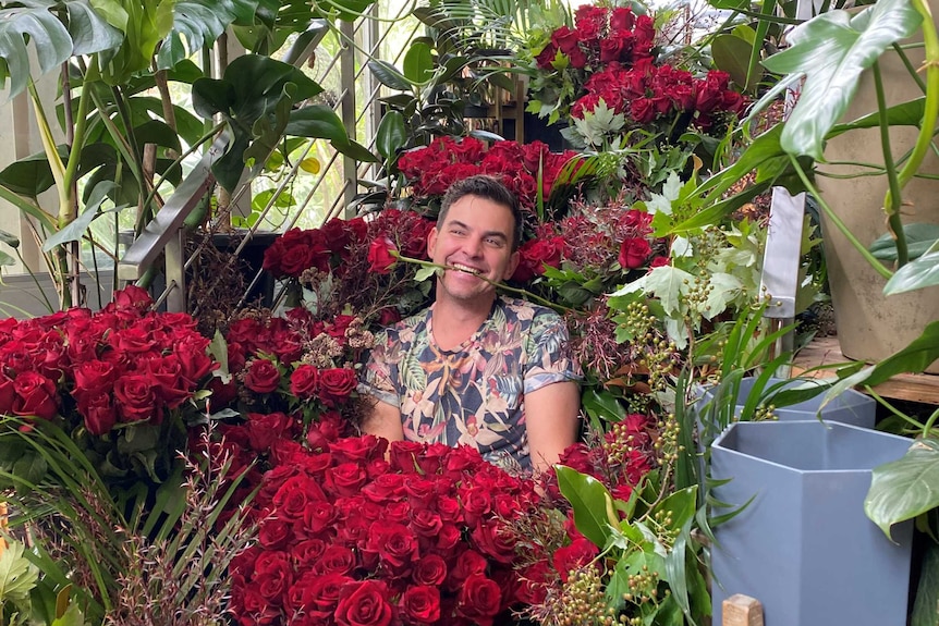 A man is sitting among hundreds of red roses and greenery in a shop