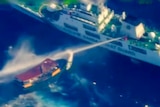A large ship blasts a smaller boat with water in open ocean