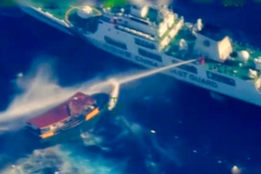 A large ship blasts a smaller boat with water in open ocean