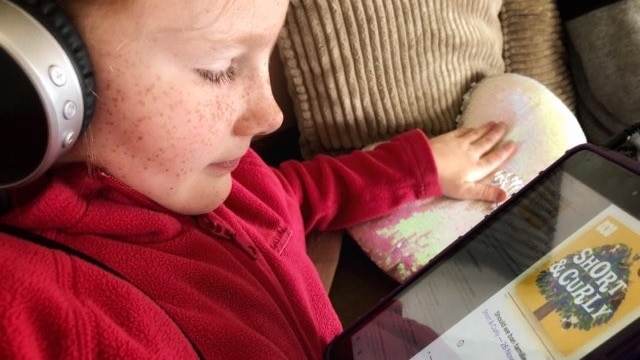 Little girl with headphones on looking at ipad with Short and Curly on screen.
