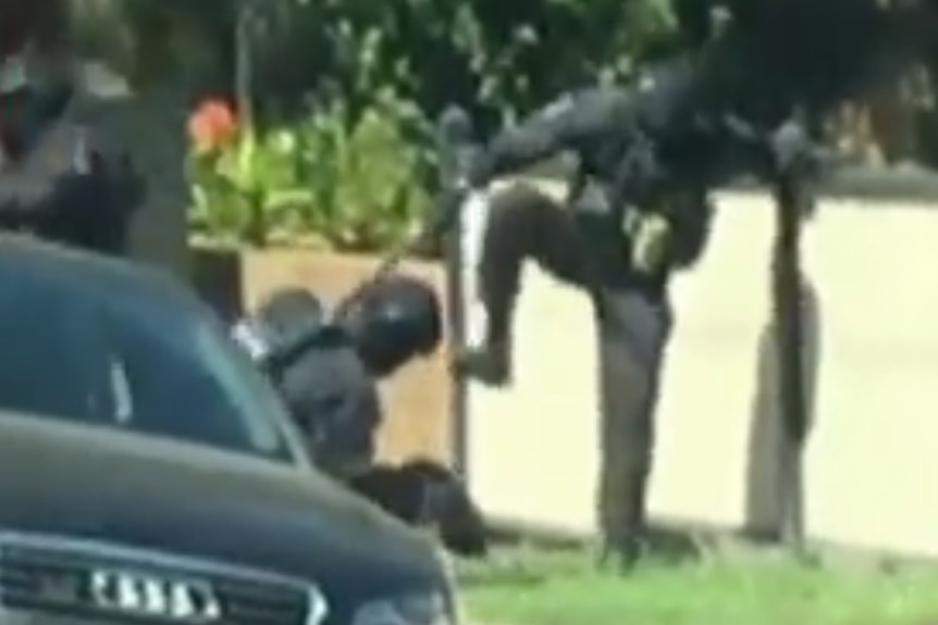 A police officer with his leg in the air, while another police officer holds a man down.