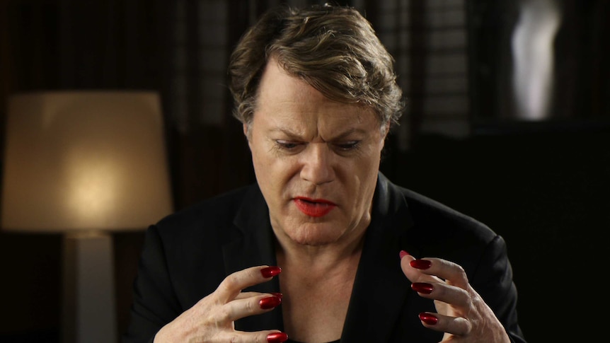 Eddie Izzard holds up his hands and concentrates while speaking.