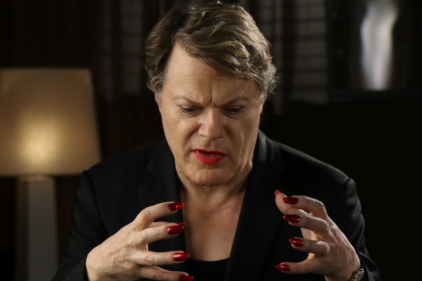 Eddie Izzard holds up his hands and concentrates while speaking.