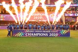 A cricket team celebrates with the IPL trophy as flames go off in the background.