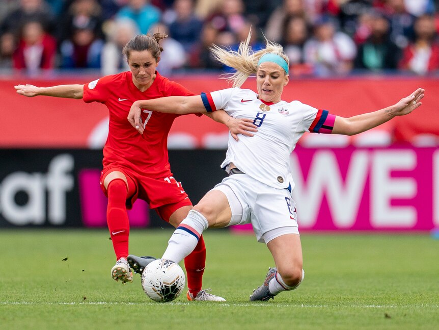 Two women soccer players, one wearing red and one wearing white, battle for the ball