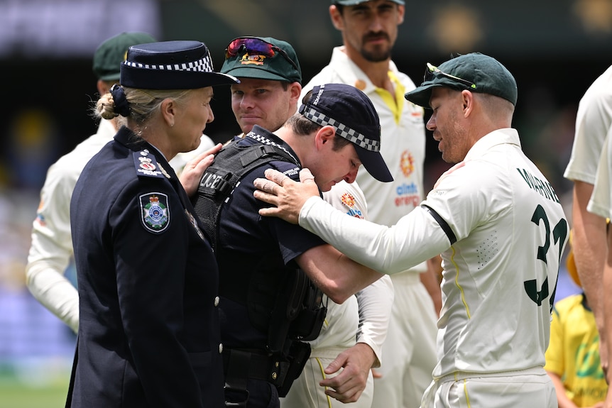 david warner consoles a member of the queensland police as does the QPS commisioner as fellow cricketers watch on