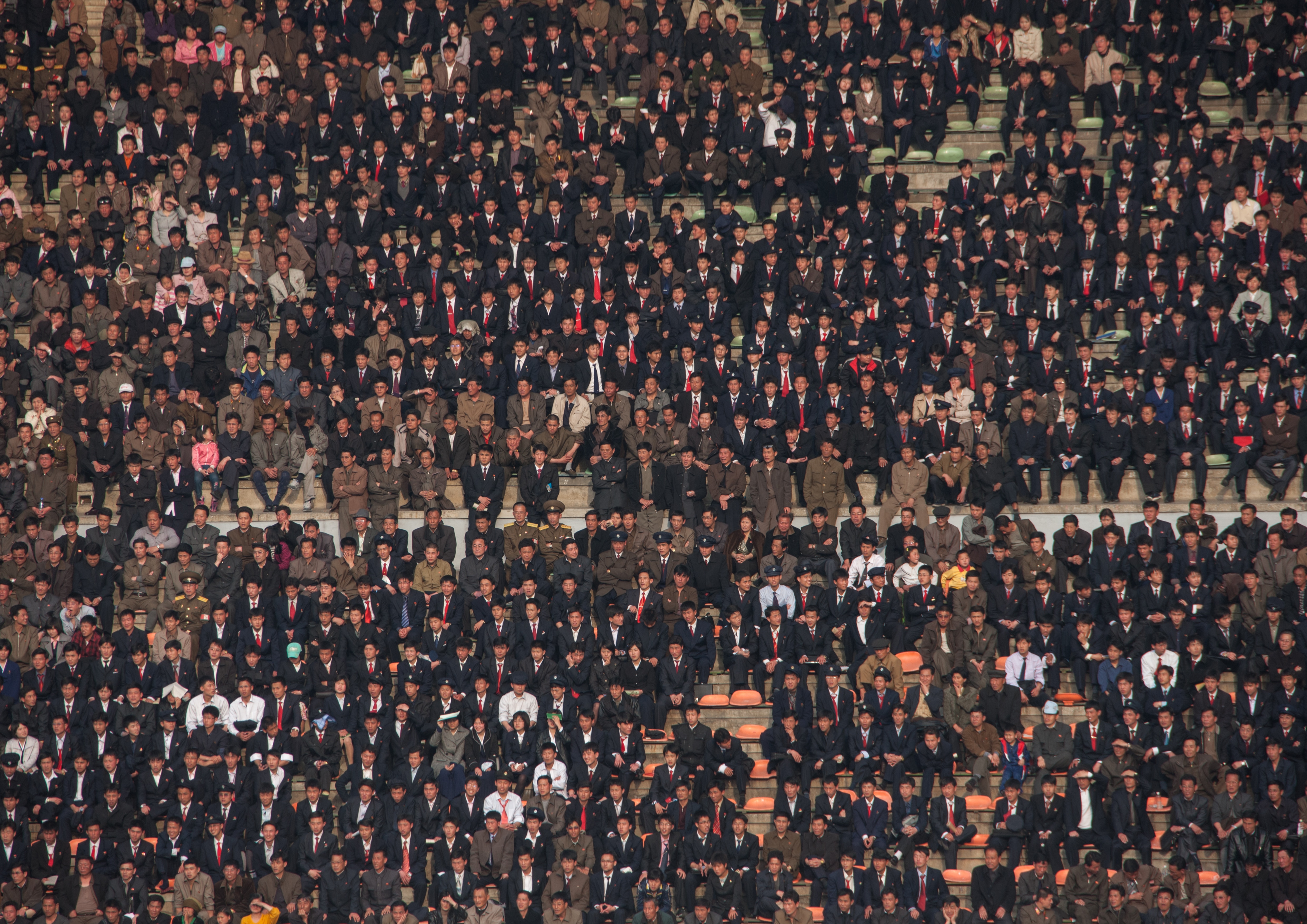 A crowd of people dressed in military and business uniforms sitting in a big stadium stand