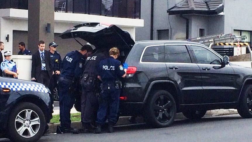 Several police officers check something in the boot of a black vehicle.