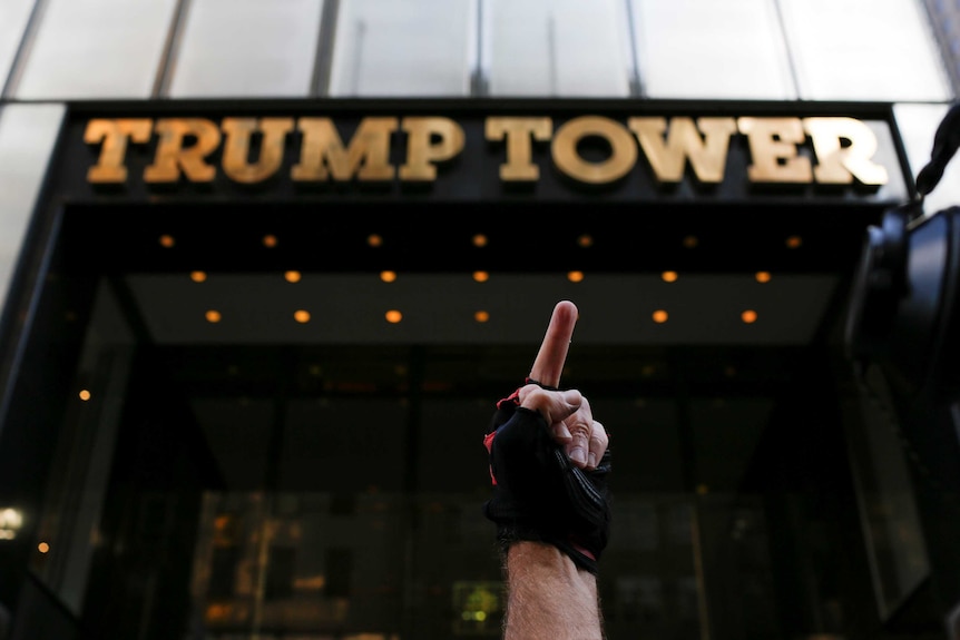 A man gives the middle finger to the Trump Building during a protest by a small group of people against the Trump administration