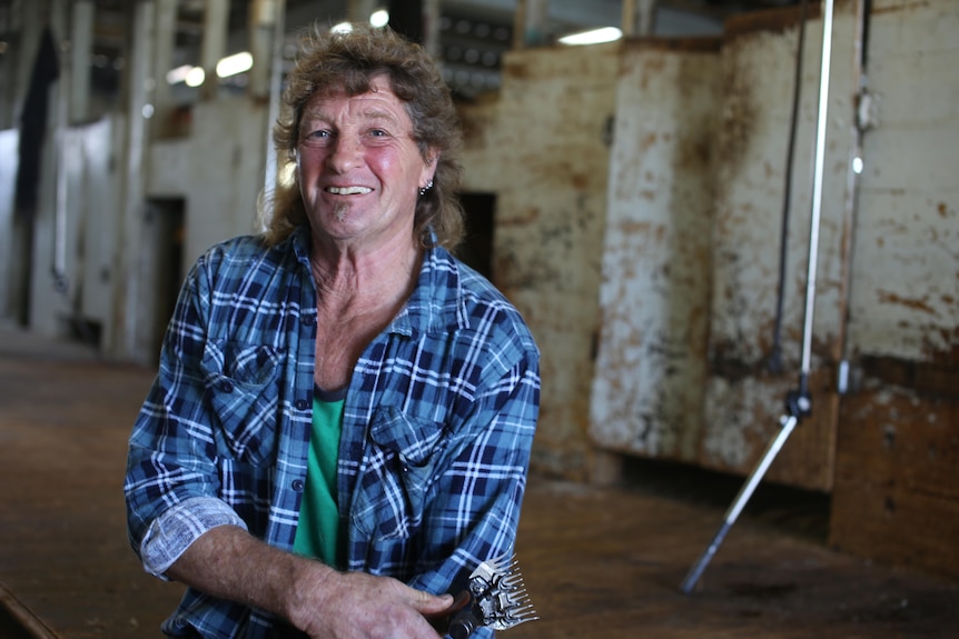 Image d'un homme tenant une tondeuse à l'intérieur d'un hangar à laine souriant à la caméra