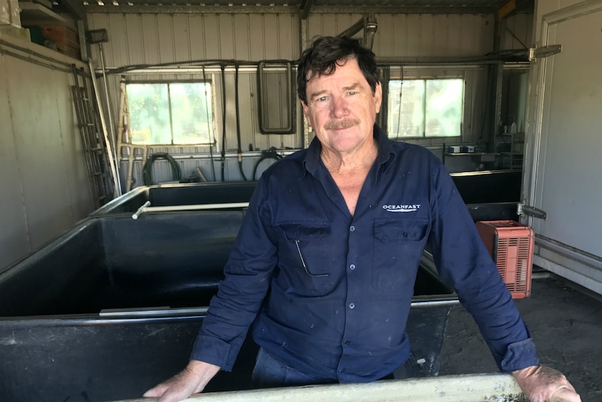 Bill Keast stands behind a water tank in his shed.