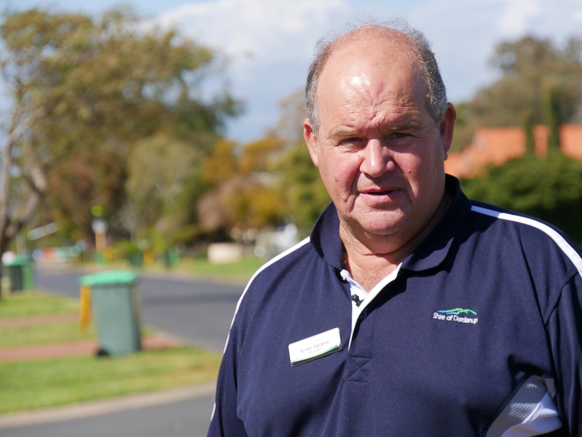 Un hombre se para frente a contenedores de basura con tapas de color verde claro.