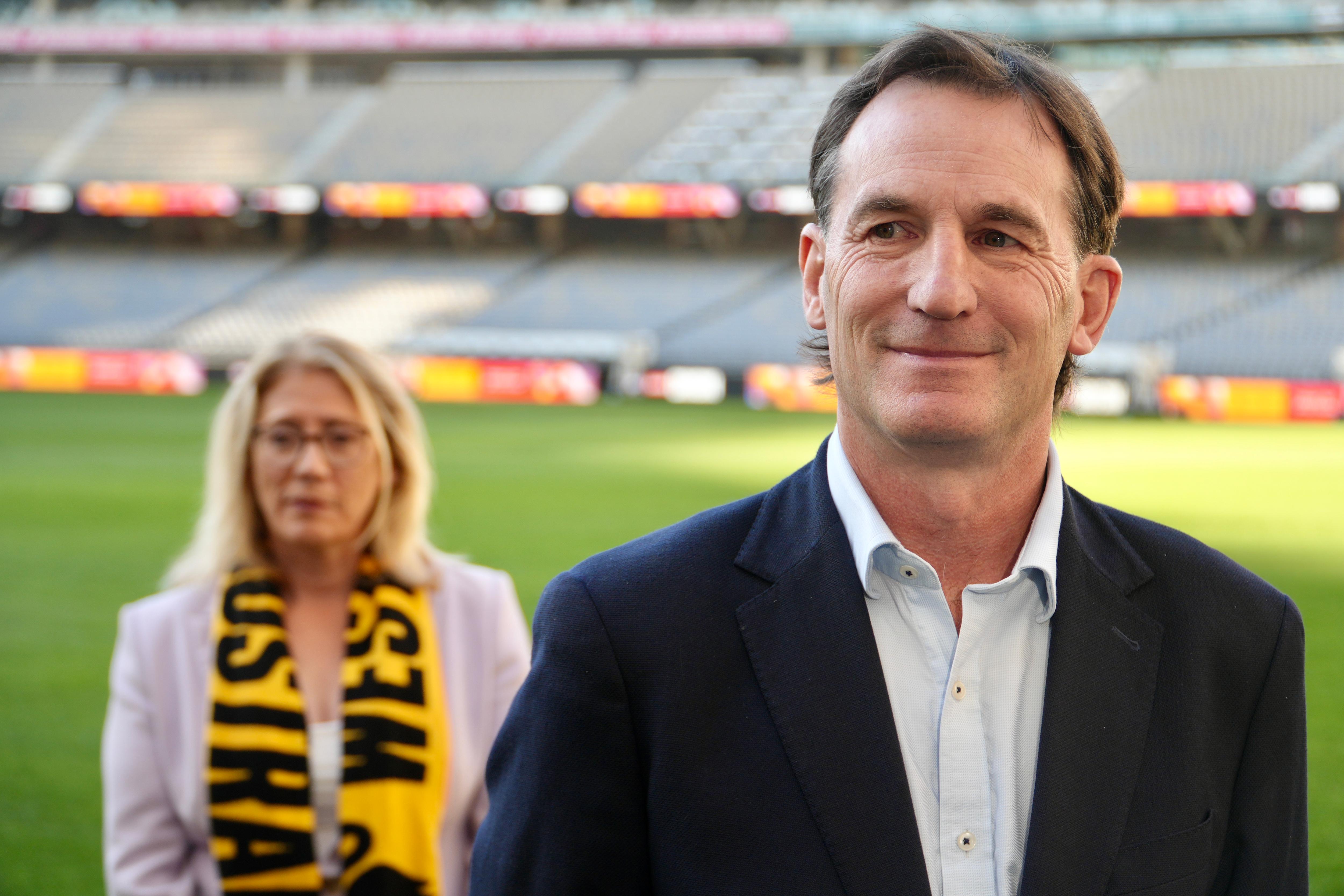 Andrew Dillon stands smiling with WA Treasurer Rita Saffioti in the background. 