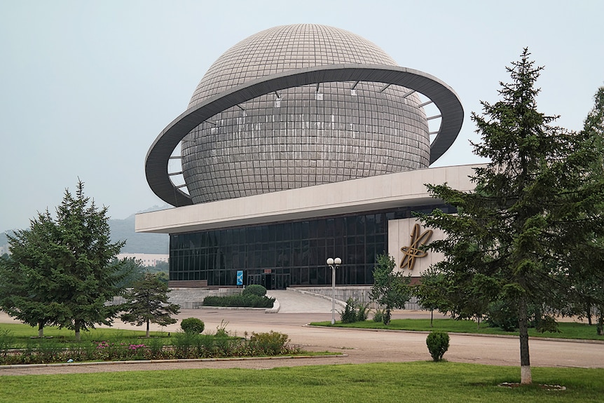 Colour photograph of a low level but long building with a large grey dome structure similar to a planet in shape, on it's roof.