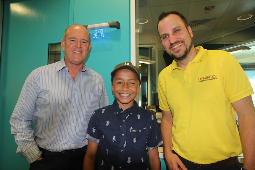 Three people smile at the camera in a radio studio.