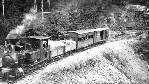 A black and white photo showing a steam-powered locomotive rounding a curve.